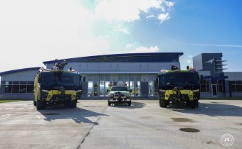 2 yellow airport fir fighting apparatus in front of an airport fire station.